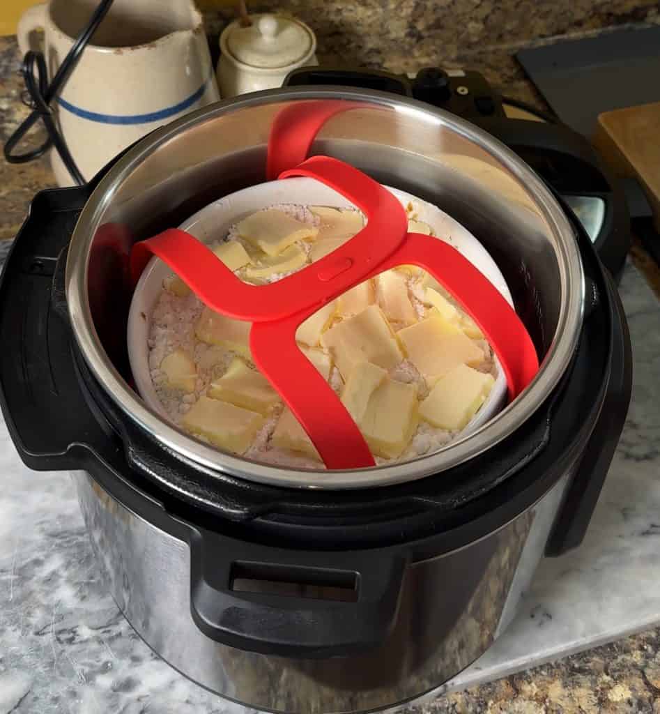 peach cobbler in a bowl sitting inside of a sling lowered into an instant pot ready to be cooked