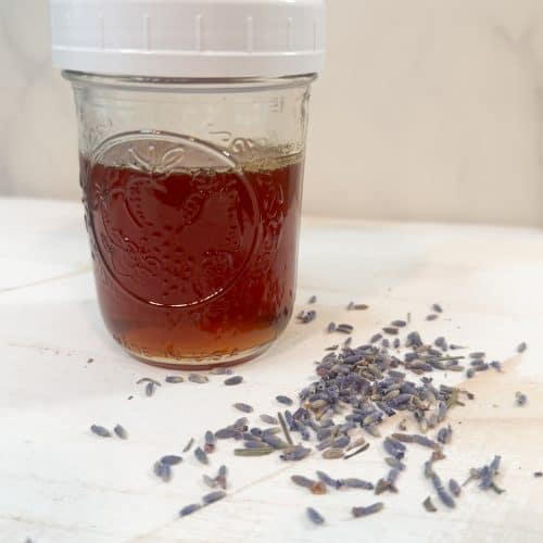 lavender infused honey in a glass mason jar sitting next to some dried lavender buds