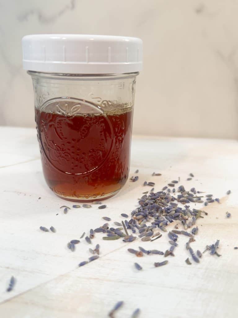 lavender infused honey in a glass mason jar sitting next to some dried lavender buds