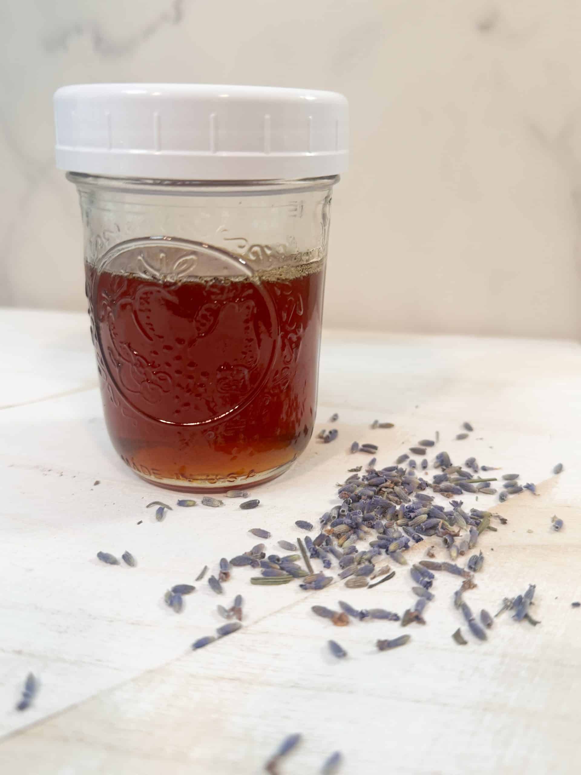 lavender infused honey in a glass mason jar sitting next to some dried lavender buds