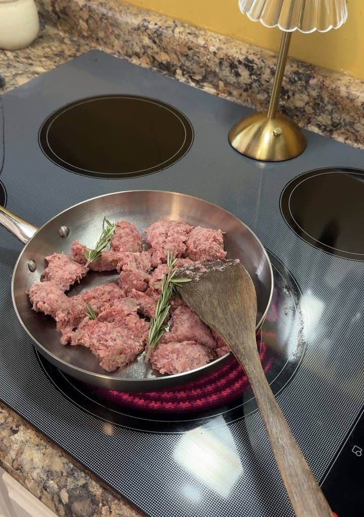 fresh sprigs of rosemary added to breakfast sausage as it cooks in a skillet