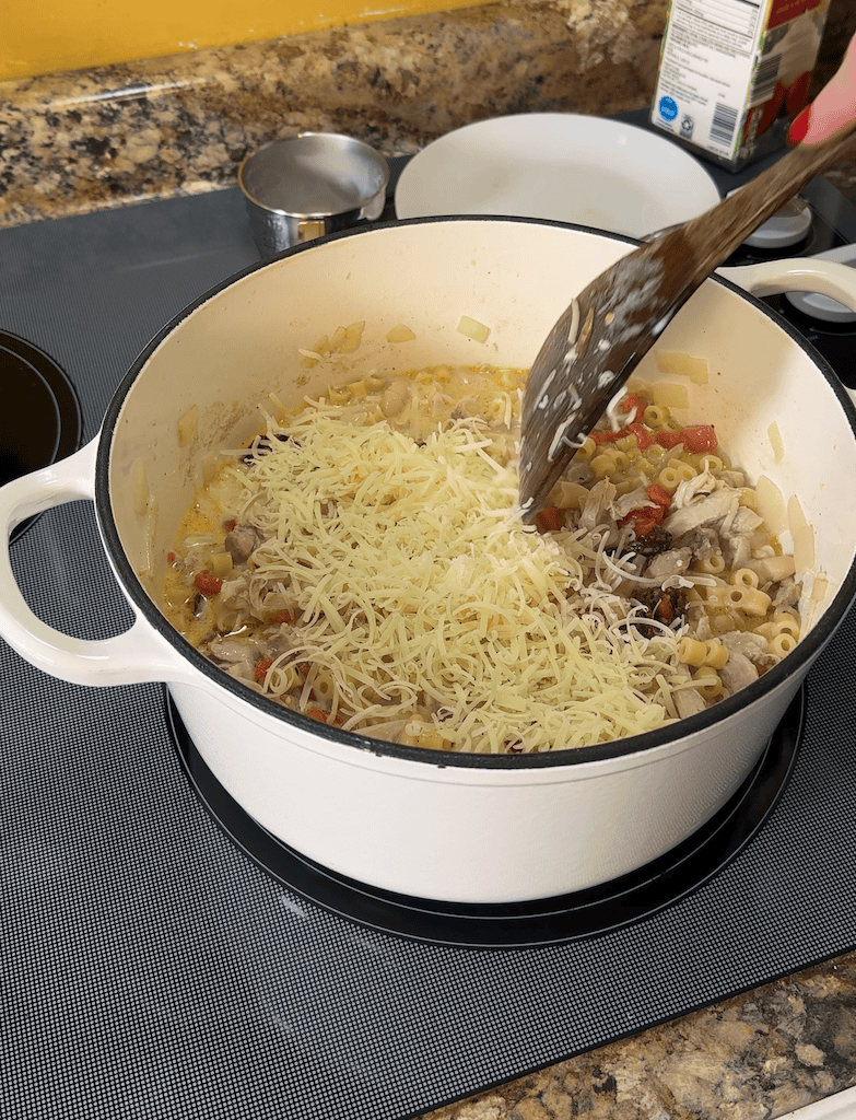 adding parmesan into the creamy tuscan chicken noodle soup