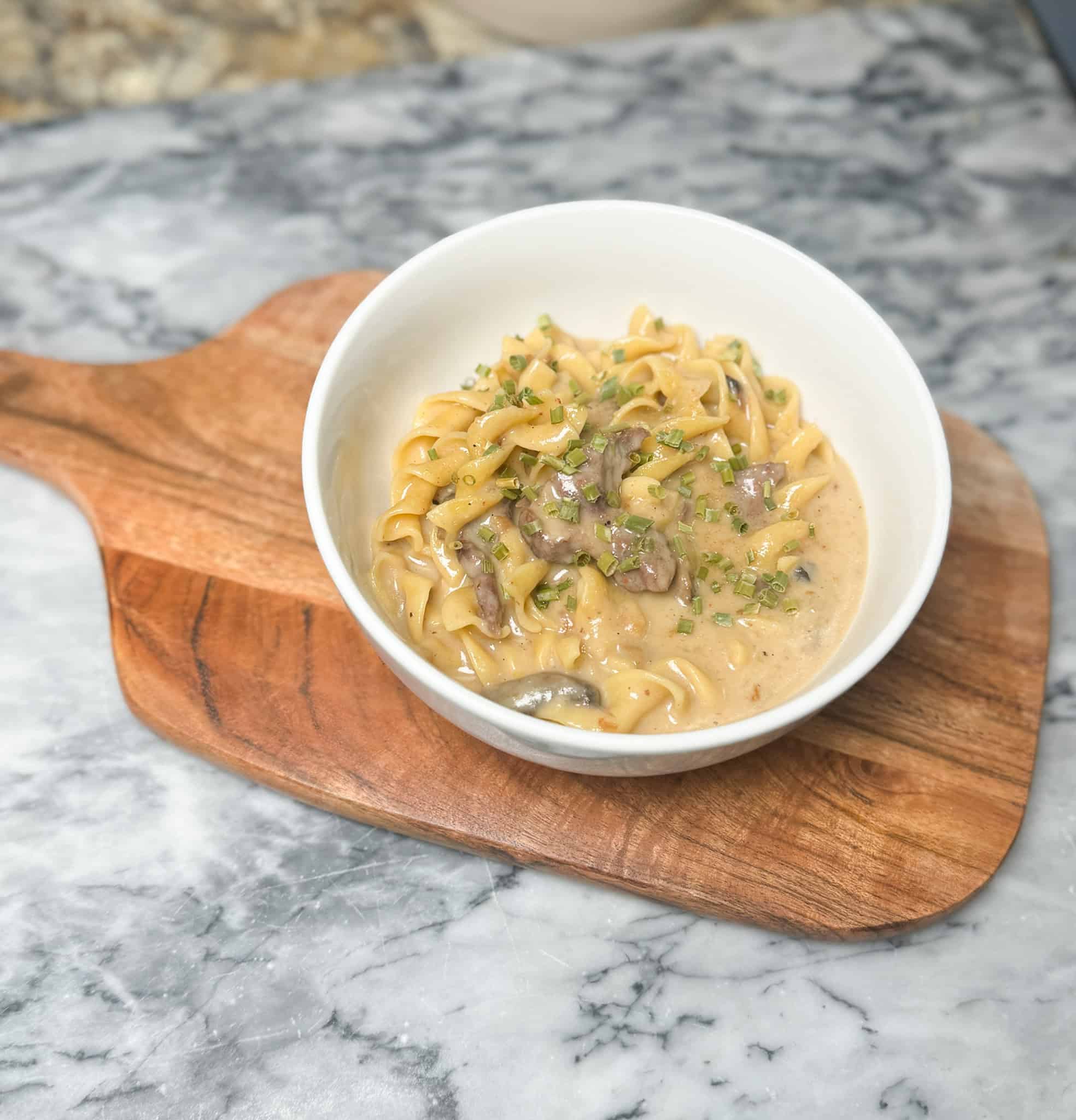 beef stroganoff in a white bowl sitting on a cutting board
