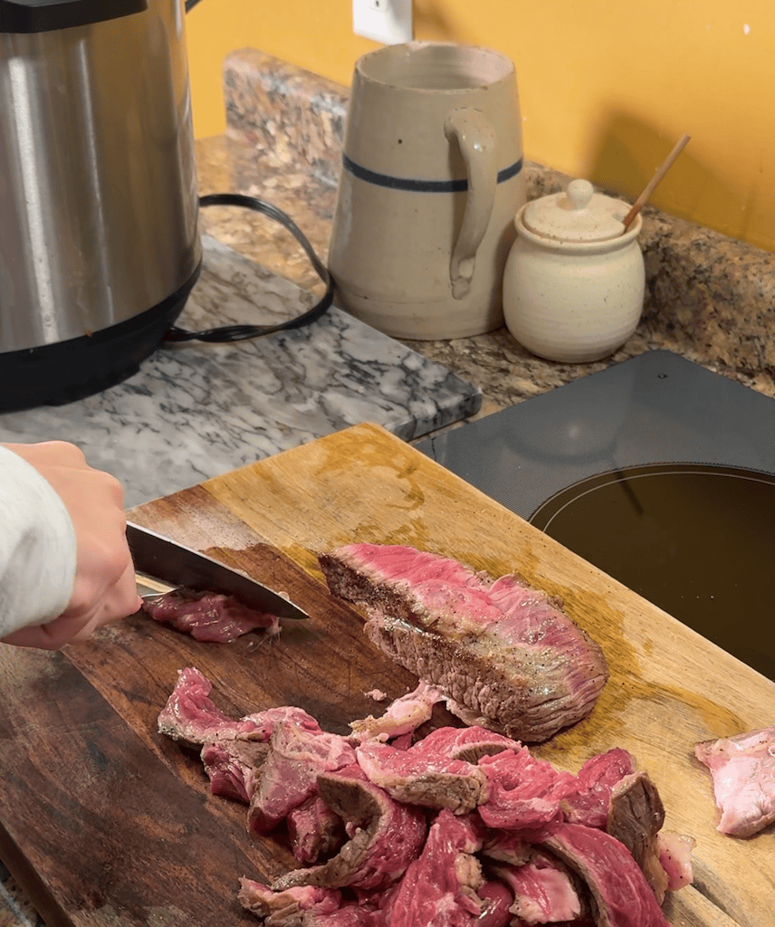 slicing a chuck roast into thin strips on a large cutting board