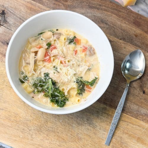 creamy tuscan chicken noodle soup in a bowl sitting next to a spoon