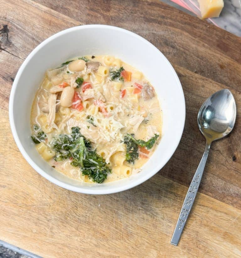 creamy tuscan chicken noodle soup in a bowl sitting next to a spoon