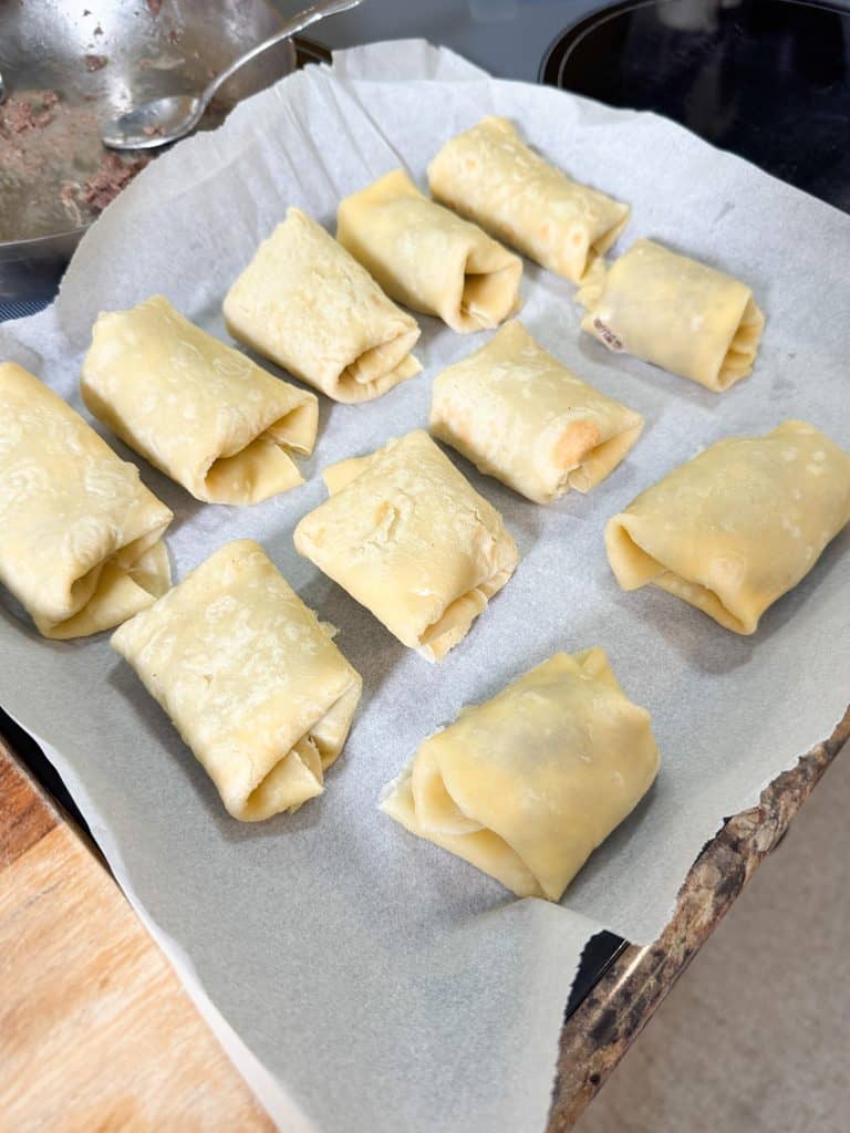 filled egg roll wrappers ready for the air fryer sitting on a parchment lined baking sheet