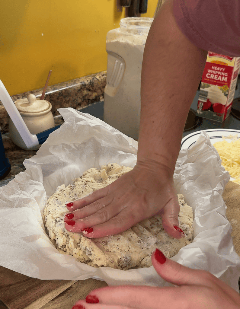 pressing the cheesy sausage and rosemary scone dough into a pie dish