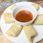 sweet and spicy chili sauce in a bowl in the middle of egg rolls