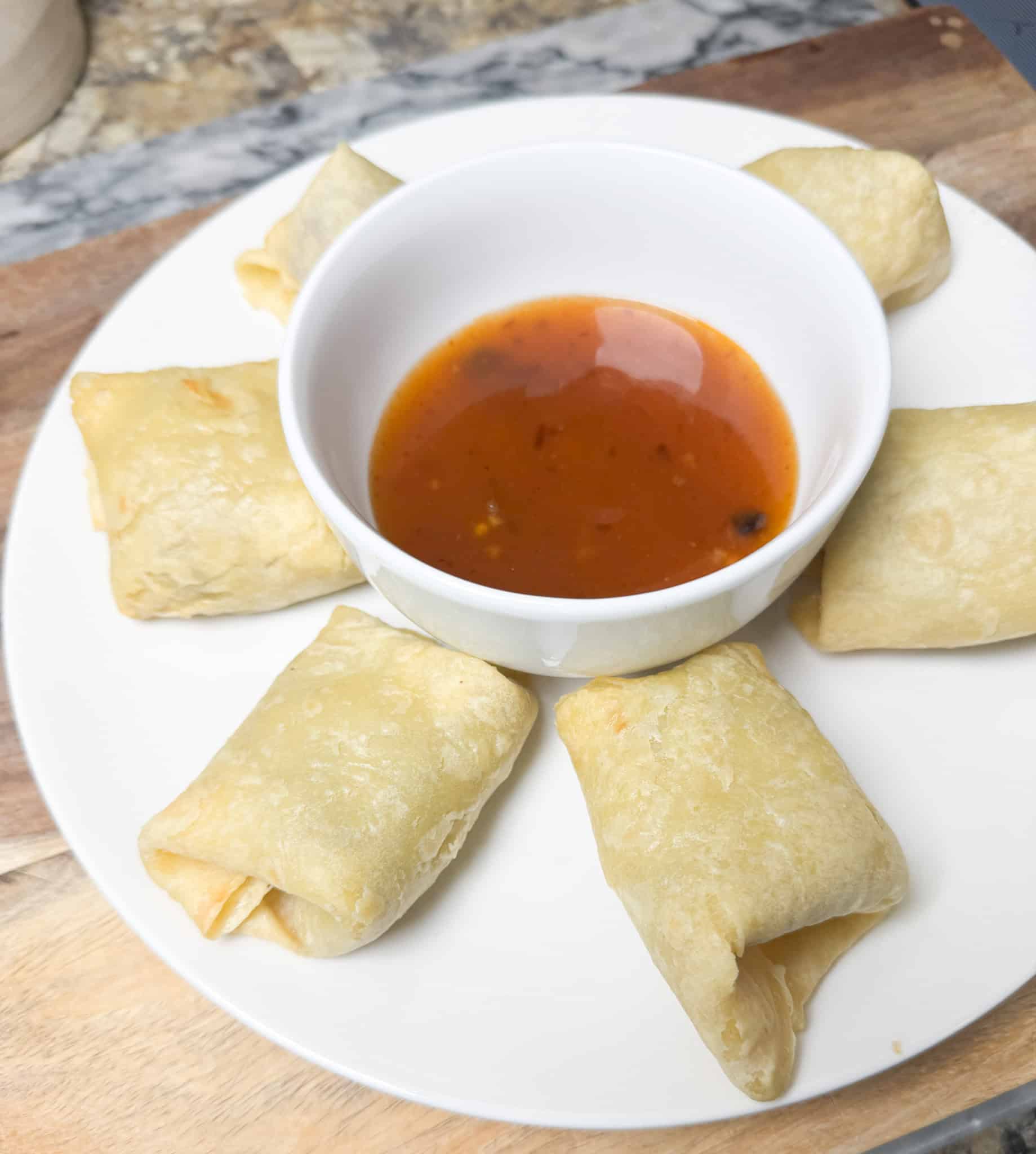 sweet and spicy chili sauce in a bowl in the middle of egg rolls