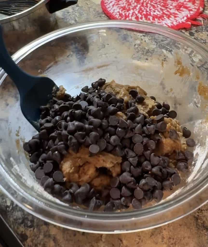 chocolate chips being added to cookie dough in a glass bowl