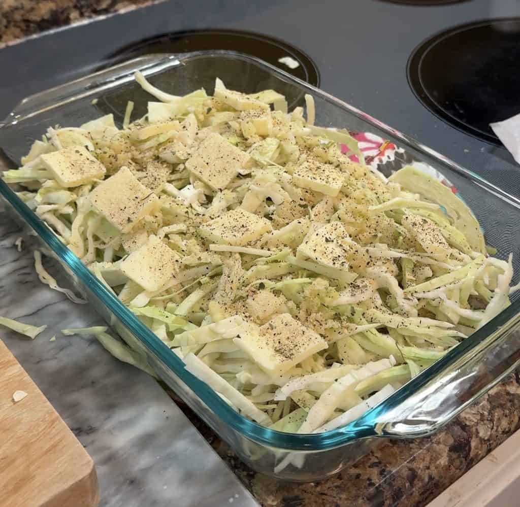 a clear 9x13 in casserole dish with thinly sliced cabbage and butter with seasoning
