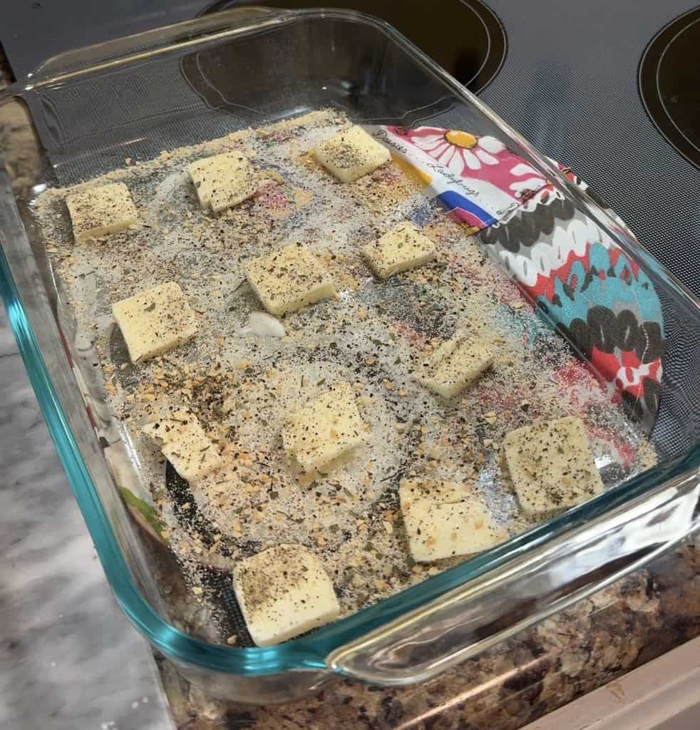 a clear 9x13 inch casserole dish with thin slices of butter and seasoned ready for the sliced cabbage