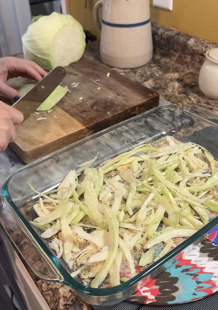 thinly slicing a small head of cabbage on a wooden cutting board