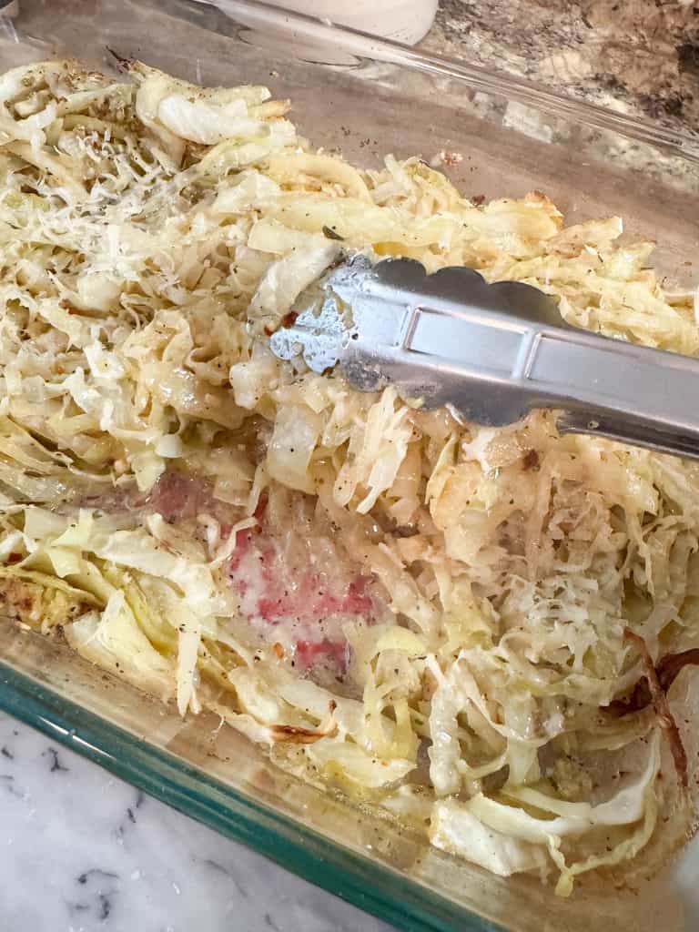 using tongs to toss buttery garlic parmesan baked cabbage